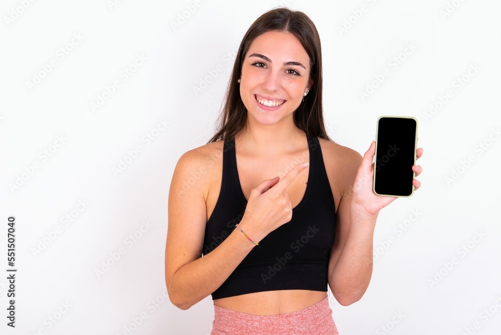 Smiling Young caucasian woman wearing sportswear over white background showing and pointing at empty phone screen. Advertisement and communication concept. Smiling Young caucasian woman wearing sportswear over white background showing and pointing at empty phone screen. Advertisement and communication concept.
