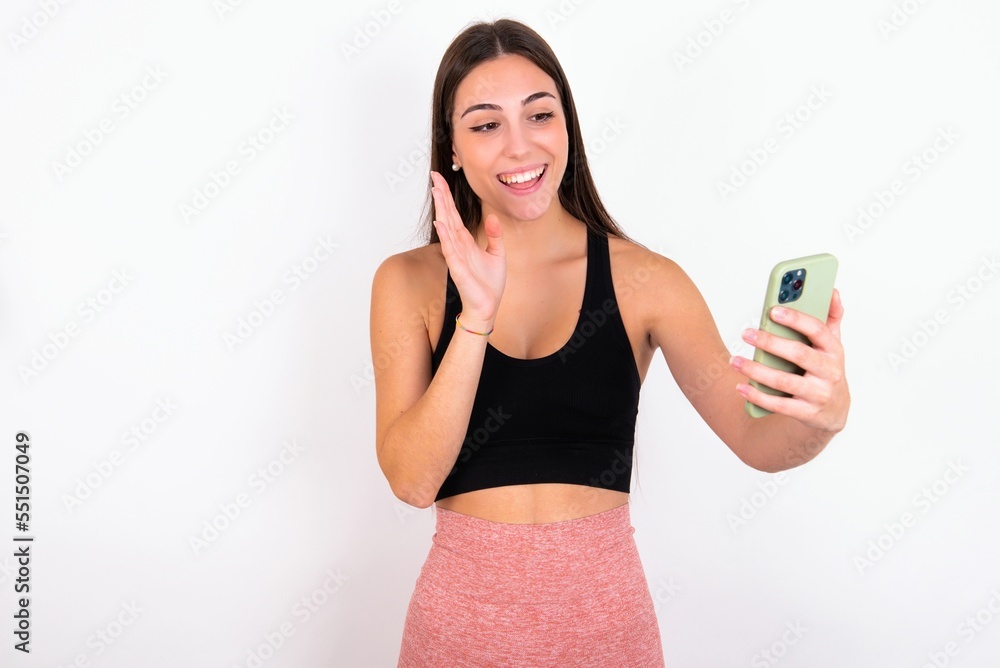 Portrait of happy friendly Young caucasian woman wearing sportswear over white background taking selfie and waving hand, communicating on video call, online chatting. Portrait of happy friendly Young caucasian woman wearing sportswear over white background taking selfie and waving hand, communicating on video call, online chatting.