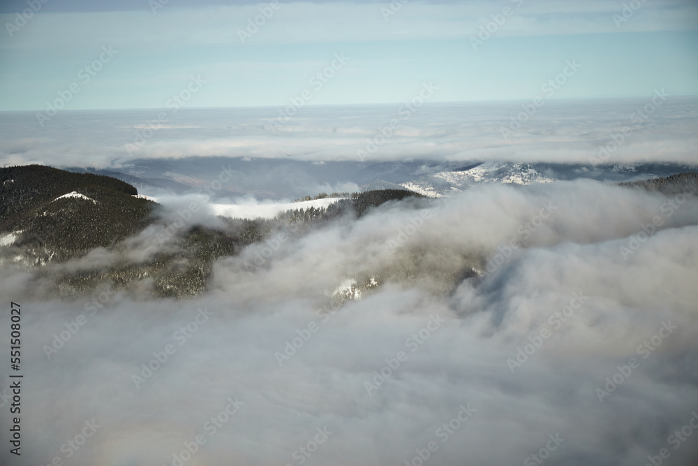 Fototapeta premium Above sea of fog in winter mountains. Sunny day in snow covered Carpathian Mountains. Clouds above clear sky