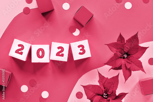 2023 Christmas festive background with viva magenta decorations on paper background. Viva Magenta is color of the year 2023. Poinsettia, cubes with numbers 2023. Trendy monochromatic background.