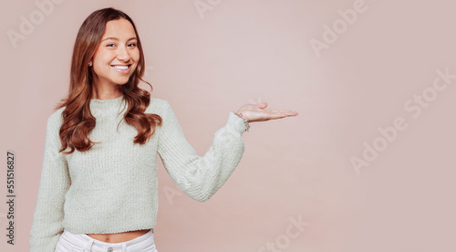 Horizontal banner of smiling young multiracial woman with curly hair, showing commercial offer with palm of hands, copy space on right, isolated over blue background.