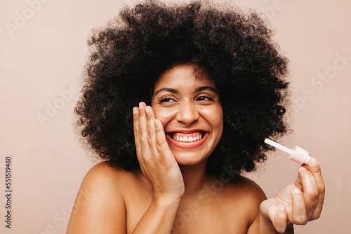 Woman with Afro hair applying cosmetic oil on her face