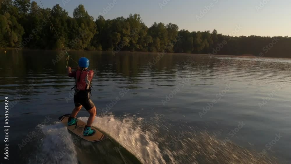 FPV drone flying following to extreme female wakeboard surfer wearing helmet riding on lake water at cable wake park on background of bright sunlight at summer sunny day. Tracking shot in slow motion. FPV drone flying following to extreme female wakeboard surfer wearing helmet riding on lake water at cable wake park on background of bright sunlight at summer sunny day. Tracking shot in slow motion.
