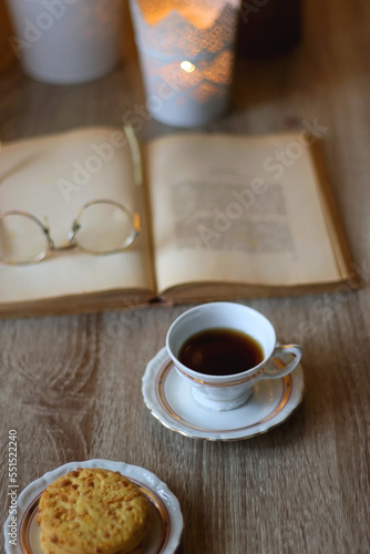 Plate with peanut butter cookies  cup of tea or coffee  open book  reading glasses and lit candles on the table. Selective focus.