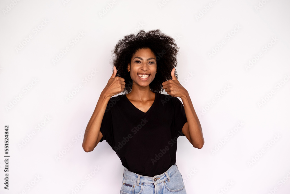 Portrait of happy young woman making thumbs up and smiling. African American lady wearing black T-shirt and jeans showing like sign against white background. Approval concept Portrait of happy young woman making thumbs up and smiling. African American lady wearing black T-shirt and jeans showing like sign against white background. Approval concept