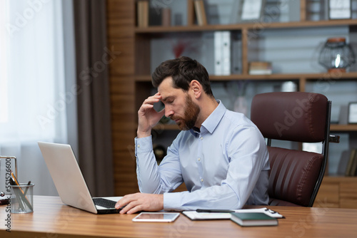 Mature pensive sad businessman working inside office, boss using laptop at work thinking about difficult decision in shirt.