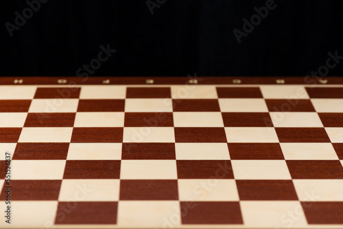 Empty wooden chessboard on a black background.