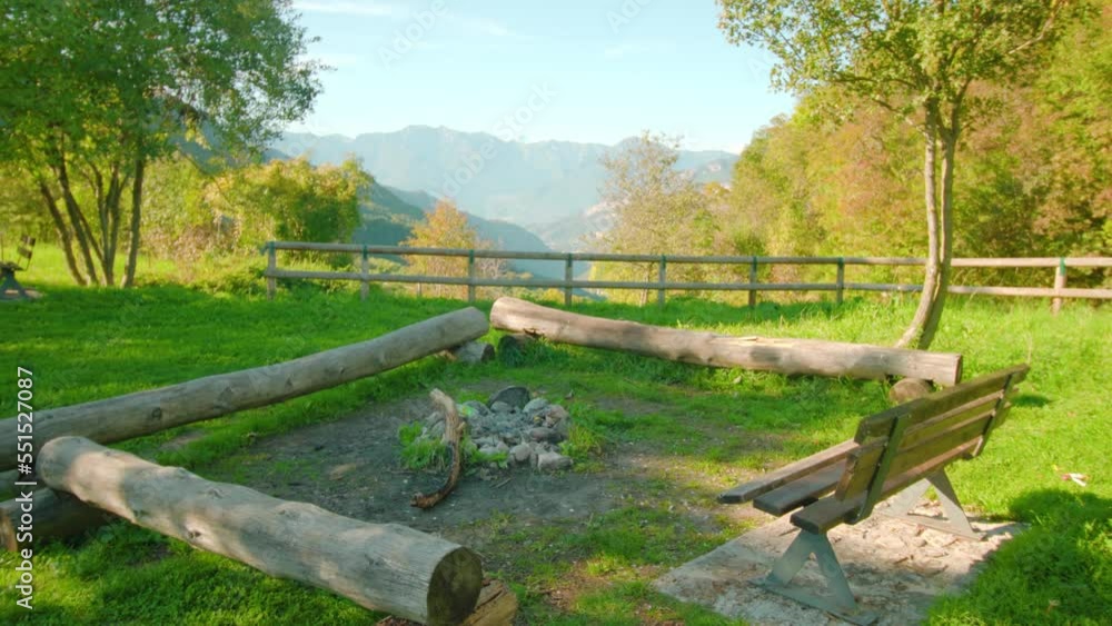 Wooden bench and seating places made of logs placed around campfire on green lawn overlooking multicolored autumn mountains in park Wooden bench and seating places made of logs placed around campfire on green lawn overlooking multicolored autumn mountains in park