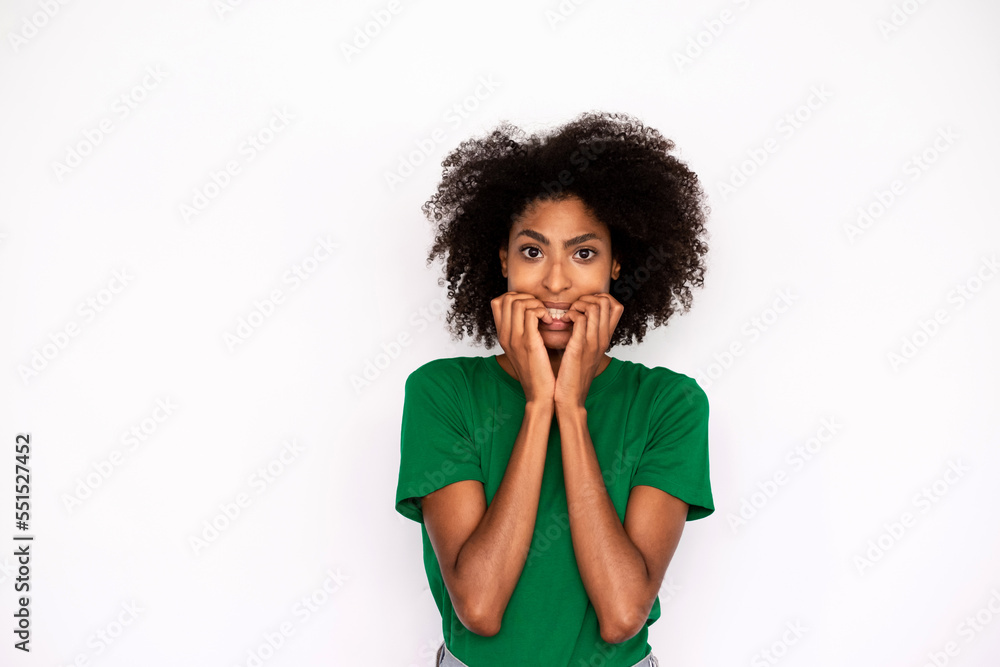 Portrait of neurotic young woman biting nails over white background. African American lady wearing green T-shirt looking at camera in anxiety. Stress and fear concept Portrait of neurotic young woman biting nails over white background. African American lady wearing green T-shirt looking at camera in anxiety. Stress and fear concept