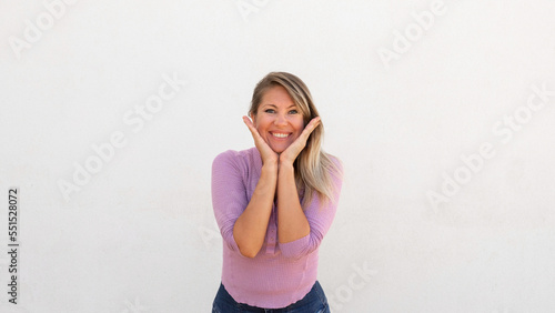 Excited Caucasian woman with hands on cheeks. Happy mature female model with fair hair in lilac blouse looking at camera with wide smile after hearing good news. Optimism  advertising concept