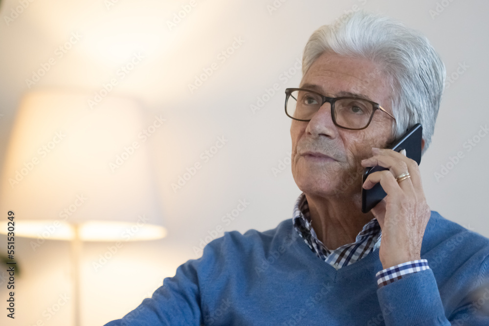 Mature businessman talking on phone at phone. Medium shot of gray-haired senior man in eyeglasses having discussion with colleague while sitting at table. Digital devices, communication concept Mature businessman talking on phone at phone. Medium shot of gray-haired senior man in eyeglasses having discussion with colleague while sitting at table. Digital devices, communication concept