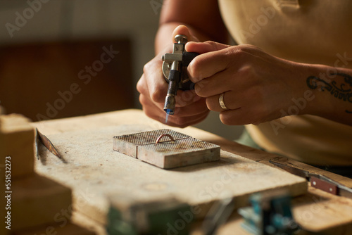 Close up of artisan jeweler welding ring at rustic workstation while creating handmade jewelry pieces, copy space