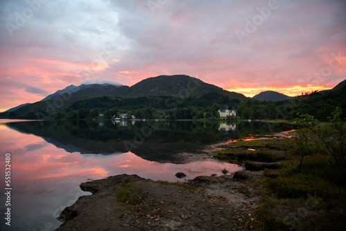 Colourful sunset in the Scottish Highlands with mountains, houses, sky and light reflected off the lake