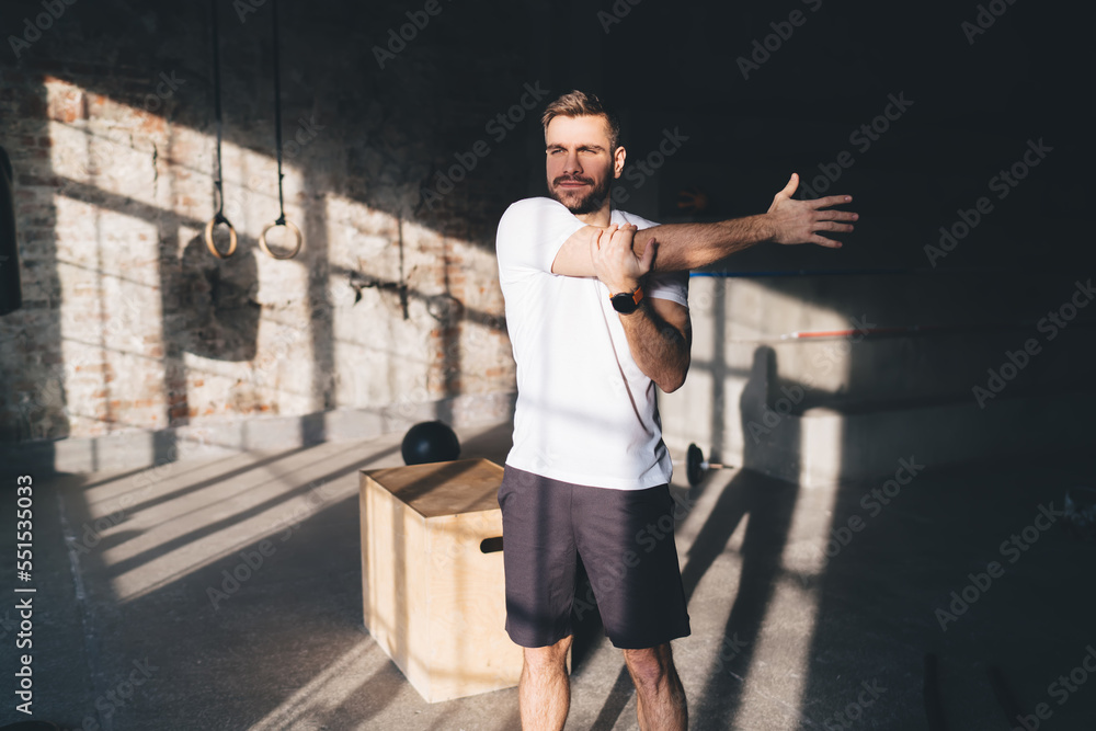 Positive sportsman stretching arms during workout at gym on sunny day