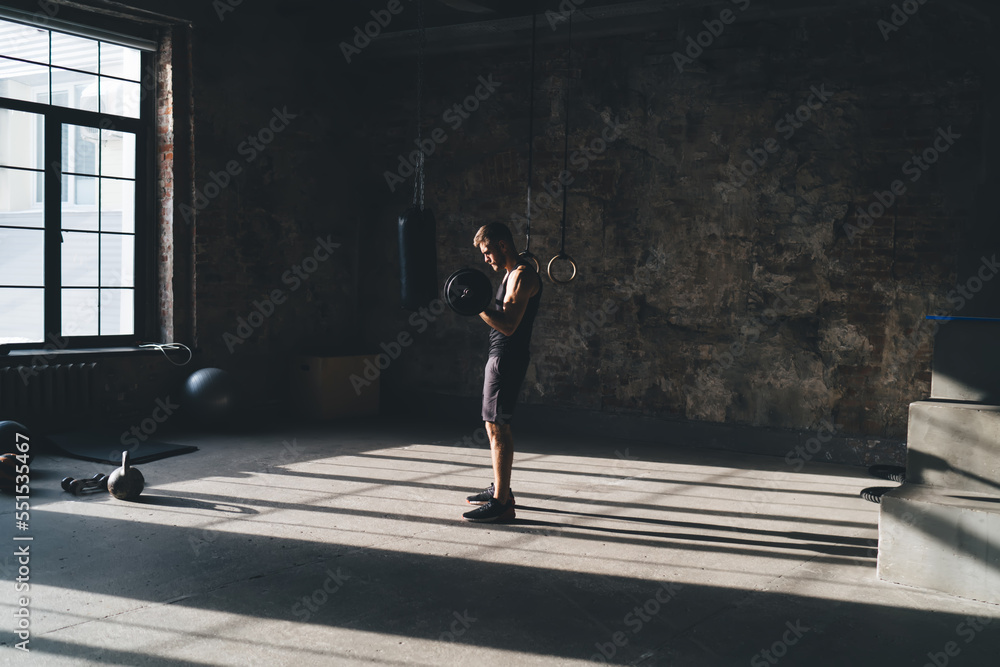 Sportive man training at gym while lifting dumbbell Sportive man training at gym while lifting dumbbell
