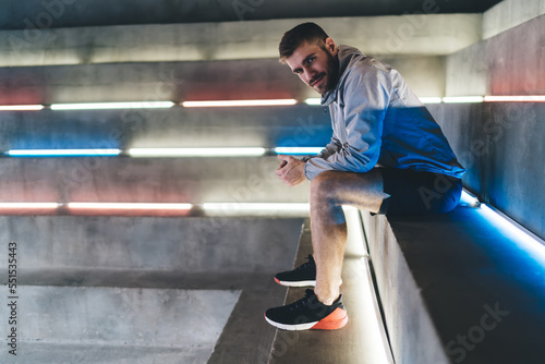 Positive young man sitting on gym stairs with lights