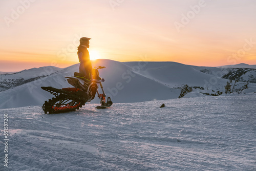 Snowbike rider standing on top of mountain during sunset with atmospheric landscape view