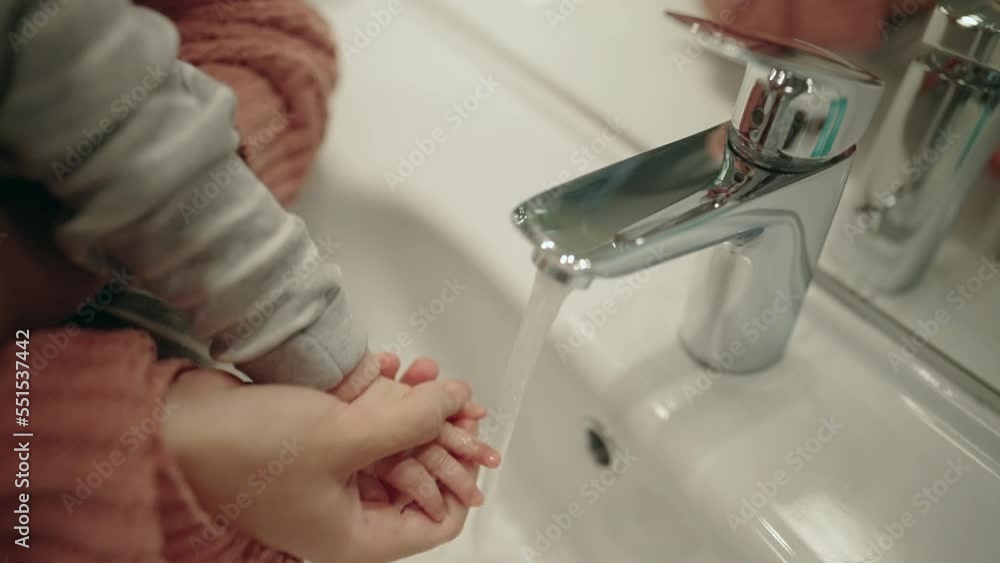 Close up - Mother cleaning baby's hand in a bathroom. Birds' perspective of a woman, holding her baby and washing her little hands Close up - Mother cleaning baby's hand in a bathroom. Birds' perspective of a woman, holding her baby and washing her little hands
