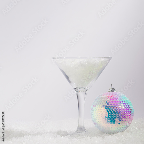 New Year disco bauble ornament and martini glass filled with snow. Snowy winter design idea. Holiday  abstract concept. Sparkling multicolored ball
