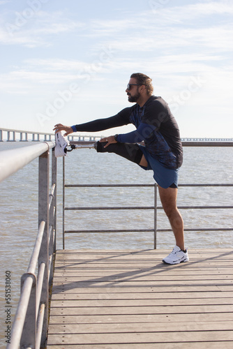 Man with mechanical leg getting ready for training on embankment. Man in sport clothes stretching leg in park on summer day. Sport, training concept