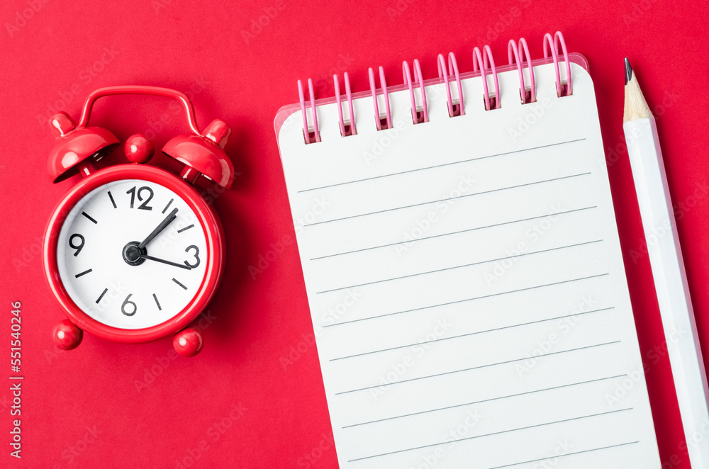 The Blank open diary and Alarm clock with pencil on red colored background The Blank open diary and Alarm clock with pencil on red colored background