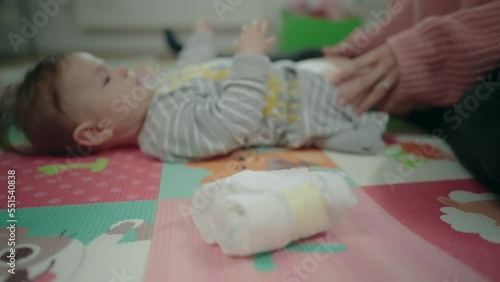 Changing diapers - Slow motion of a baby girl lying on the floor while mother changes her diaper and puts the used one in front of the camera