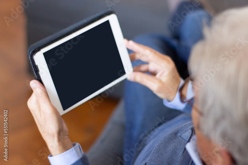 Busy man reading article on tablet. Over shoulder view of senior man holding digital device and sitting on sofa. Gadget concept