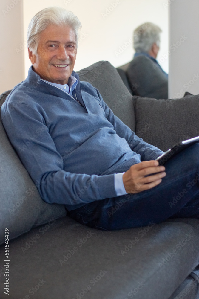 Portrait of smiling senior man with tablet. Positive aged man with gray hair resting in living room. Retirement concept Portrait of smiling senior man with tablet. Positive aged man with gray hair resting in living room. Retirement concept
