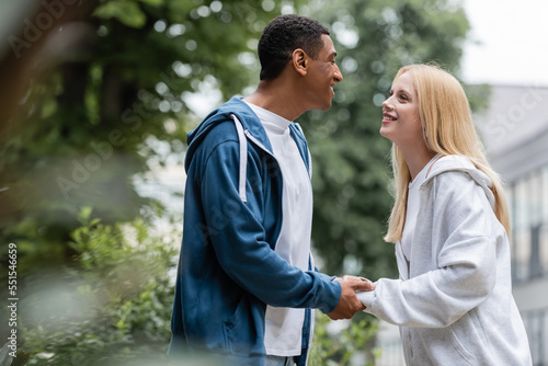 side view of blonde woman and african american man smiling at each other and holding hands outdoors © LIGHTFIELD STUDIOS
