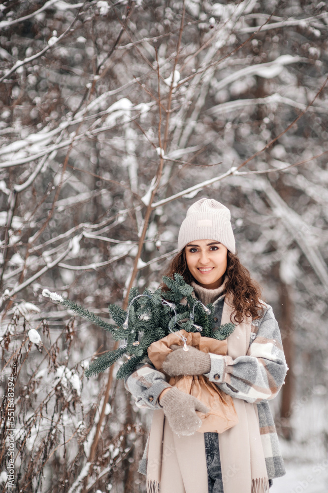 A stylish young woman in a hat stands in a snowy forest with branches of fir nobilis in a craft package A stylish young woman in a hat stands in a snowy forest with branches of fir nobilis in a craft package