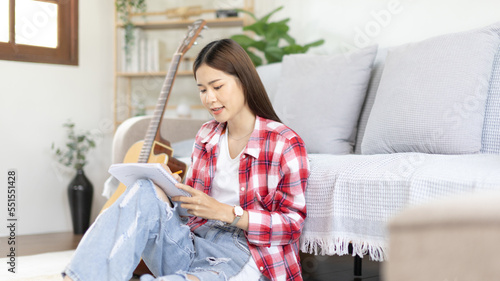 Asian woman specializes in music is composing the lyrics and melody for the opening of a new single  Using imagination and concentration in creating music  acoustic guitar  Creation of music notes.