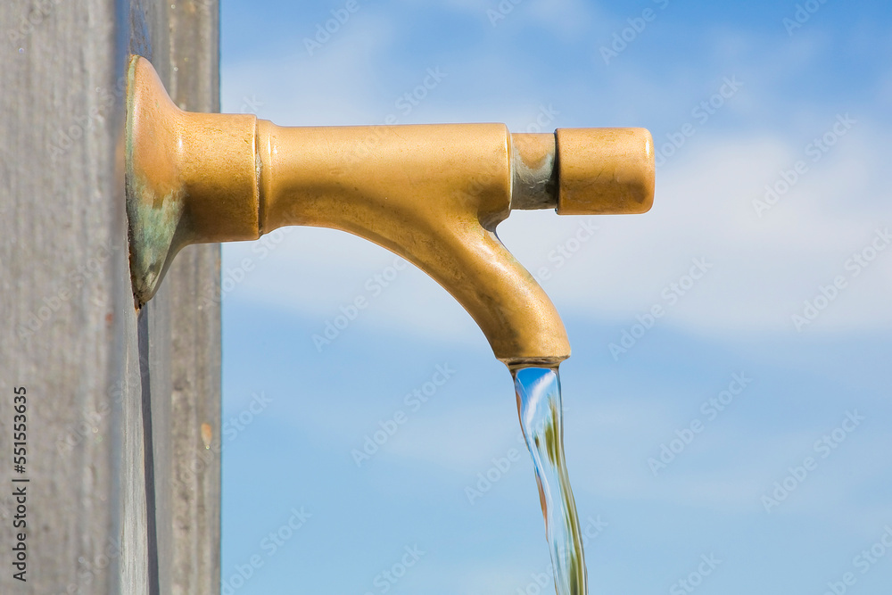 Detail of a old water brass faucet with drinking water running down in a public park with hand pushing the button