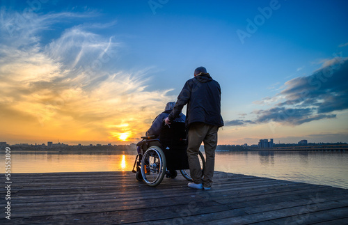 Tableau sur toile An elderly woman in a wheelchair looks at the sunset on the lake