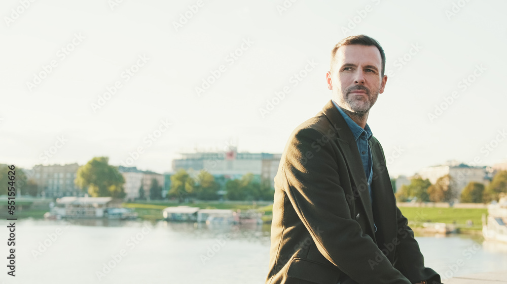 Man looks around while sitting on the embankment on the background of the river Man looks around while sitting on the embankment on the background of the river