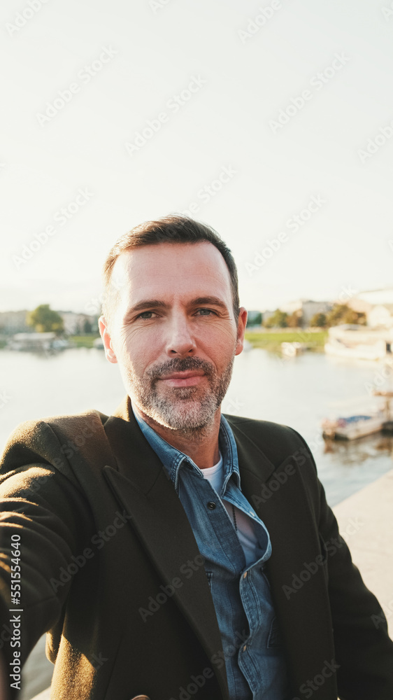 Fototapeta premium Close up, man makes selfie on mobile phone on the embankment of the river. Backlight