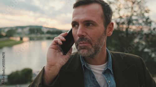 Close up, man talking on mobile phone while standing on the embankment of the river