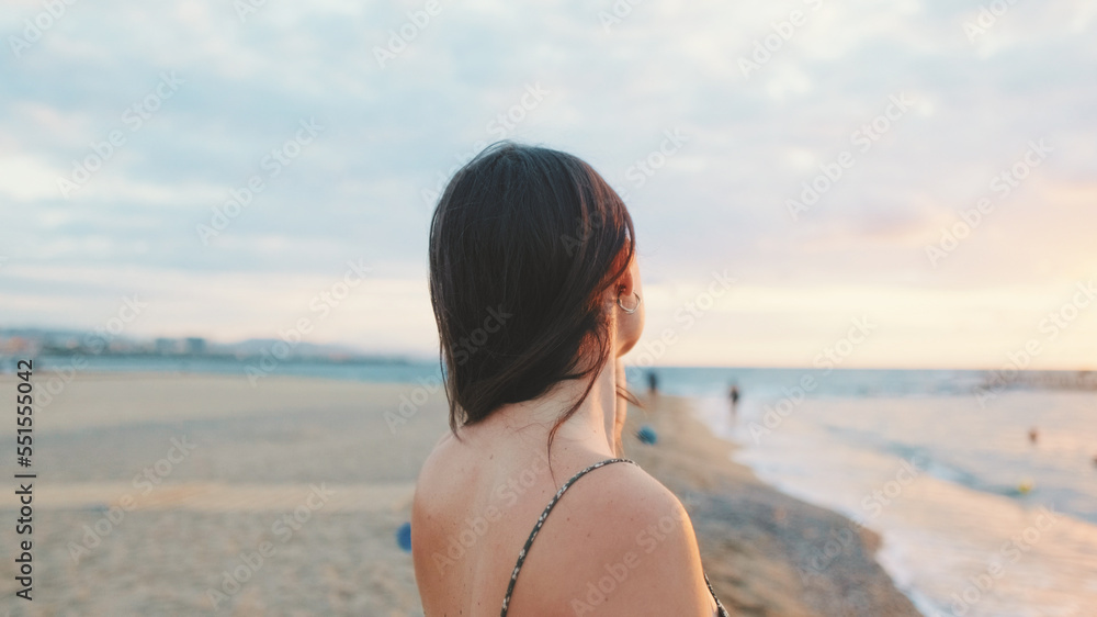 Young woman standing on the beach looking at the sunrise. Back view