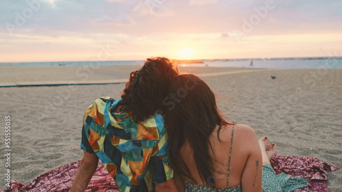 Man and woman hugging each other by the beach and watching the dawn. Back view