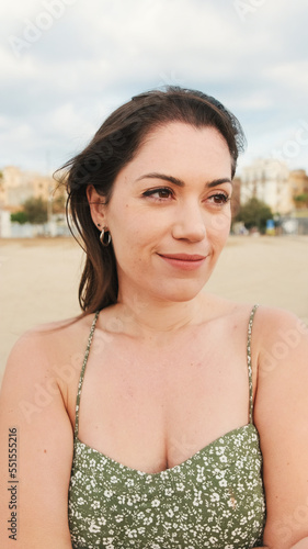 Young woman stands on the beach and looks far away. Girl turns her head, looks at the camera and smiles