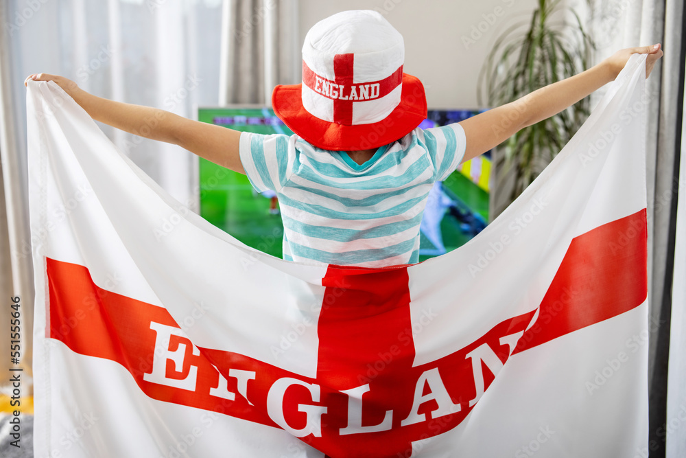 Fototapeta premium A boy holding England flag and watching soccer game on TV at home