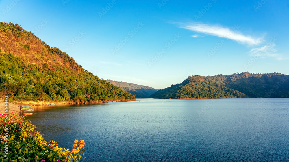 VIew of long-tailed boat floating on blue river in mountain with green forest. River in Khun Dan Prakan Chon Dam in Thailand. Landscape. Tourists on a boat to enjoy scenery in evening. Tourism concept