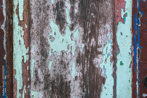 Colorful craquelure of the delaminated paint on wooden door background. Wooden texture background with old paint peels. Weathered wood. Cracked old paint with several layers. Shabby wooden wall.