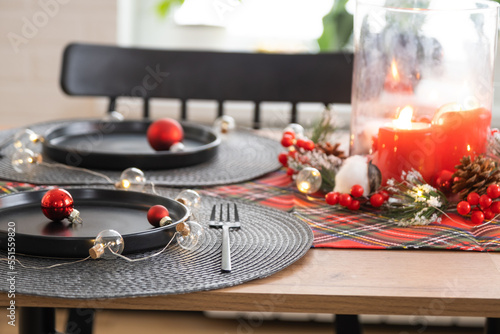 Festive table set in the living room for Christmas and New year in loft style. Christmas tree  black plates and forks  woven napkins  trendy tableware  cozy interior of the house