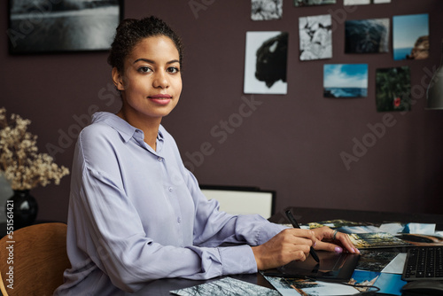 Portra of posive young woman using graphic tablet when editing photos for client photo