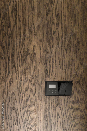 Thermostat mounted on oak wall. Modern programmable thermostat. Efficient automated heating system concept. Aesthetic temperature control panel design.