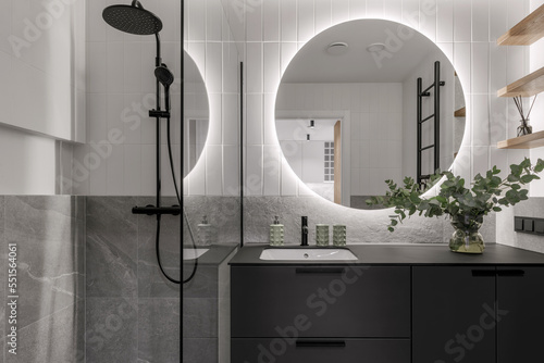 Fotografiet Modern minimalistic bathroom interior design with grey stone tiles, black furniture, eucalyptus in glass vase, round mirror