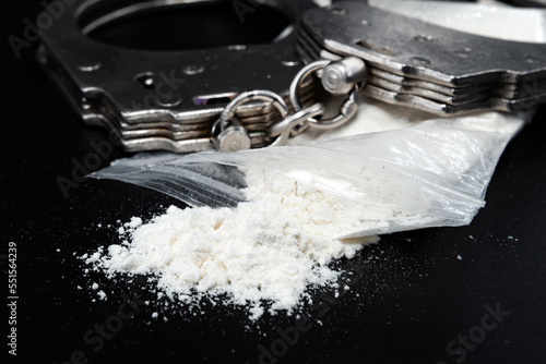 Handcuffs with drugs in a bag on a black background close-up. Law. A crime