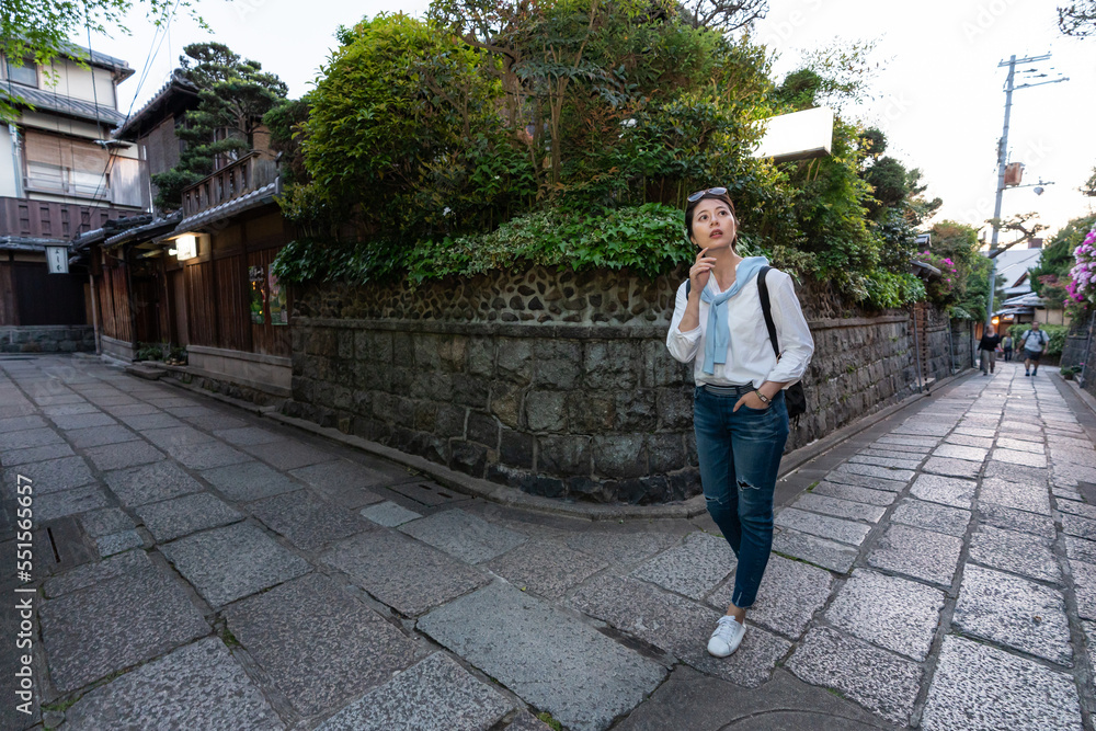 full length of lost asian Japanese female traveler looking around surroundings with hand on chin at the corner of rock pavement during her visit at Ninenzaka and Sannenzaka in Kyoto japan