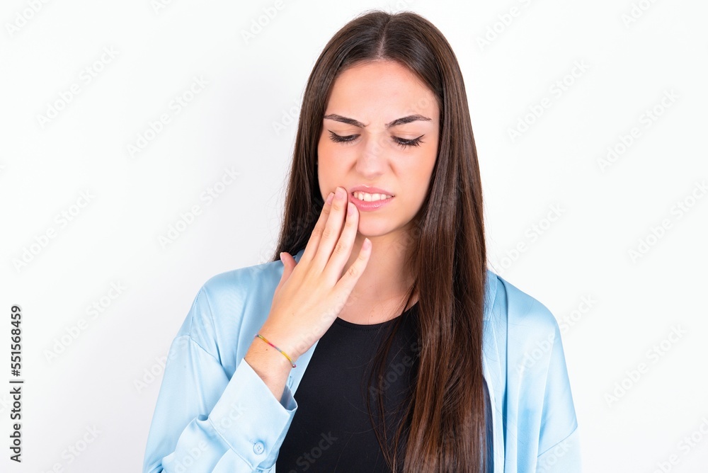 Young caucasian woman wearing blue overshirt over white background touching mouth with hand with painful expression because of toothache or dental illness on teeth. Young caucasian woman wearing blue overshirt over white background touching mouth with hand with painful expression because of toothache or dental illness on teeth.