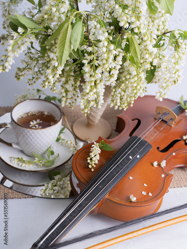 Artistic still life with a bouquet of bird cherries, a cup of tea and a violin. Vertical photo.